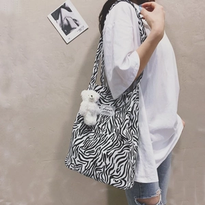 Detail of zebra print canvas tote bag with Augur label and plush bear charm