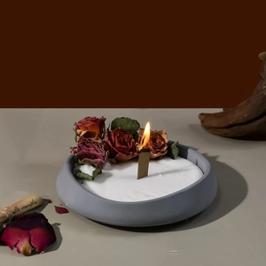 Detalle de vela de cerámica gris con rosas secas rojas y mecha de madera natural