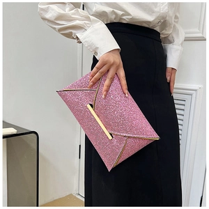 Détail d'une pochette enveloppe rose à paillettes avec bordure dorée tenue par un modèle