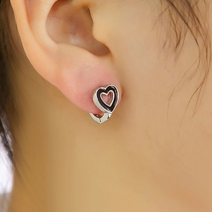 Gros plan de boucles d'oreilles cœur argentées avec accents noirs portées à l'oreille