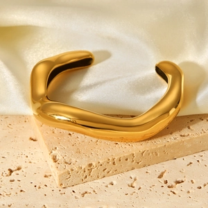 Golden irregular wavy open bangle in polished stainless steel on a beige stone