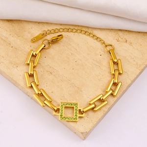 Detail of gold rectangular link bracelet with green zircon pendant on marble