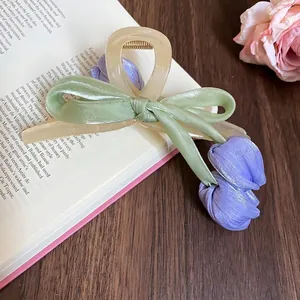Elegant acrylic tulip bow hair claw clip with silk ribbons on vintage book background