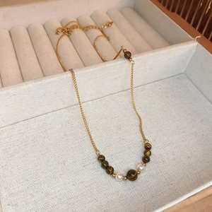 Close-up of golden necklace with tiger eye beads and pearls in a beige velvet gift box