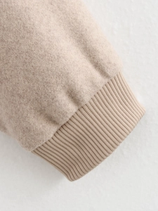 Detailed close-up of oatmeal tweed fabric texture and ribbed knit cuffs on the casual jacket
