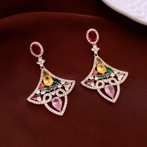 Macro detail of fan-shaped gold earrings with vibrant multi-color gemstones on brown velvet