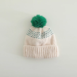 Détail du bonnet en tricot avec pompon vert et motif jacquard sur base crème douce