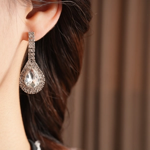 Close-up of sparkling waterdrop rhinestone earrings worn by model on a soft background