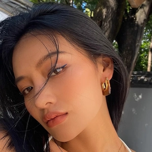 U-shaped geometric resin and gold metal hoop earrings worn by a model in nature