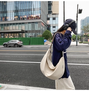 On-street view of a cream oxford canvas crossbody bag showing large capacity and drape