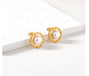 Detail of twisted gold earrings with white pearls on a textured white stone surface