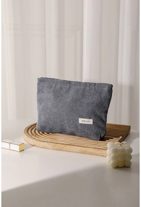 Detail of grey corduroy makeup bag on a wooden tray with a lipstick and a bubble candle