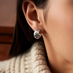 Close-up of silver geometric pleated hoop earrings worn by model with knit sweater