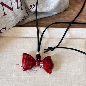 Close-up of a red resin bow pendant necklace with a black cord on a textured tray