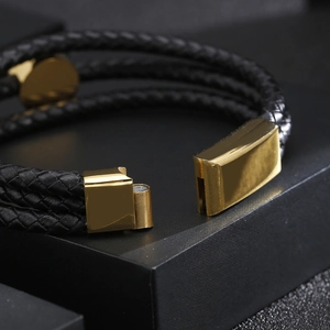 Macro shot of gold magnetic clasp and three-strand braided black leather bracelet