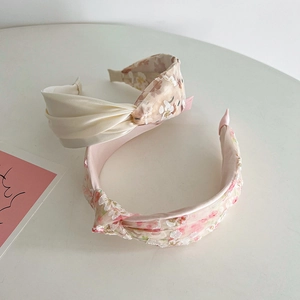 Pink floral embroidery and beige pleated mesh wide headbands on white surface