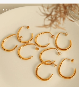 Detailed view of four pairs of polished gold C-shaped earrings on a white ceramic plate