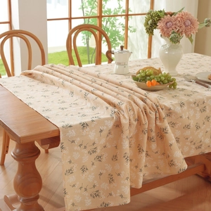 Detail of beige cotton linen tablecloth with white floral pattern on a wood table