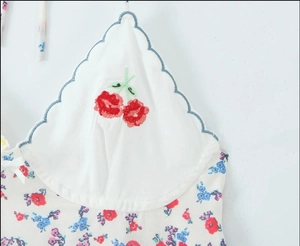 Détail d'un haut en maille blanc avec broderie cerise, imprimé fleuri et nœud