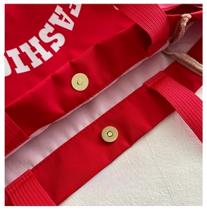 Detailed macro view of the metal magnetic snap closure on a red canvas tote bag