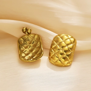 Gros plan de boucles d'oreilles géométriques dorées matelassées sur tissu soyeux