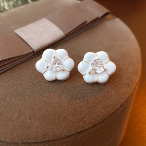 Close-up of heart-shaped zircon flower earrings with white enamel petals on velvet