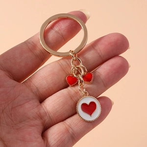 Detail of hand holding a golden keychain with red heart charms and round white enamel pendant
