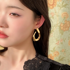 Close-up of golden irregular twisted U-shaped hoop earrings on a model