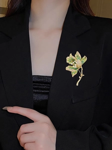 Detail of luxury gold flower brooch with green enamel and pearls on a black blazer