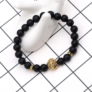 Detail of black matte bead bracelet featuring a gold lion head charm on a hand model