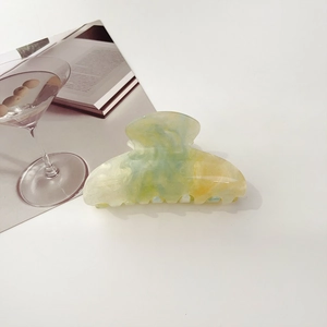 Detail of green-yellow gradient marble hair claw with gold glitter on white background