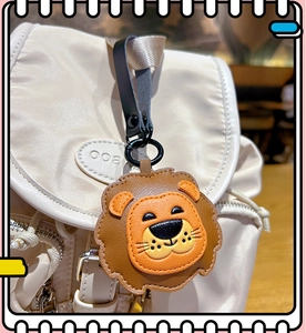 Close-up of a cute brown leather lion keychain hanging on a beige nylon backpack