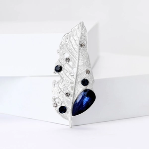 Detail of silver leaf brooch with blue and clear crystals on minimalist background