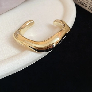 Detailed view of an irregular wave-shaped gold cuff with a high-polish metallic finish