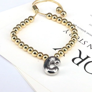 Detail of gold beaded bracelet featuring a silver letter C charm and adjustable slide clasp