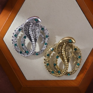 Baroque cobra snake brooches in silver and gold with green crystal accents on velvet
