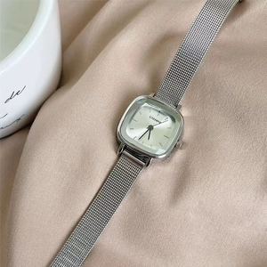 Detail of silver square dial watch with mesh strap on soft pink silk background