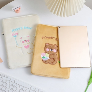 Detail of embroidered plush tablet sleeves in cream and brown on a cozy desk setup