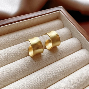 Macro detail of matte gold C-shaped earrings with brushed metal texture in jewelry tray