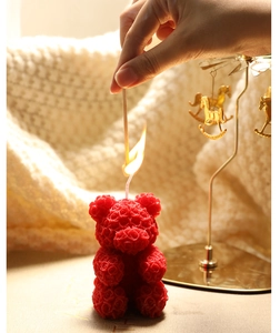 Close-up of a red rose bear scented candle being lit in a cozy, warm home setting