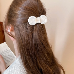 Close-up of pearl white resin bow hair clip worn on brown hair for an elegant look