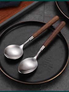 Detail of two retro stainless steel spoons with walnut wood handles on a dark plate