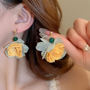Close-up of floral tassel earrings featuring gold and green fabric petals with beads