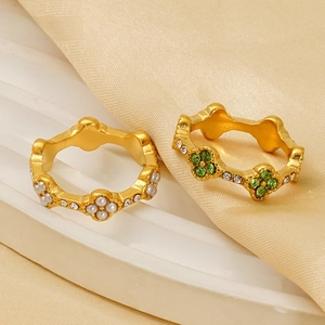 Detail of gold clover rings with white pearl and green gemstone on beige silk