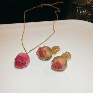 Detail of rose gold necklace and earrings set with preserved dark pink roses on tray