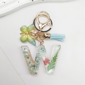 Detail of letter W keychain with real dried flowers, gold foil, butterfly and blue tassel