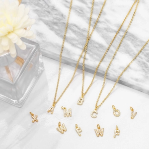 Detail of gold plated letter pendants with micro-pave crystals on marble background