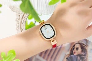 Détail d'une montre ovale or rose avec lunette en strass et bracelet cuir rouge au poignet