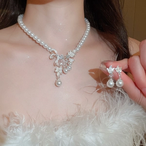 Close-up of pearl necklace and bow earrings set with rhinestones on a female model
