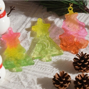 Glittery gradient resin Christmas tree pendants on a festive background with pine cones